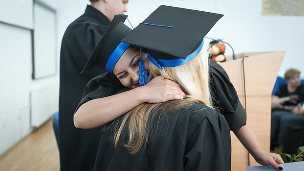 Two women hugging wearing graduation gowns
