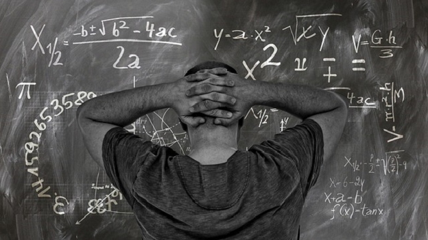 Man with head in hands in front of a chalk board showing difficult maths