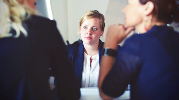 Mulher em reunião entre duas pessoas | Como o RH pode ajudar a promover a qualidade de vida no trabalho?